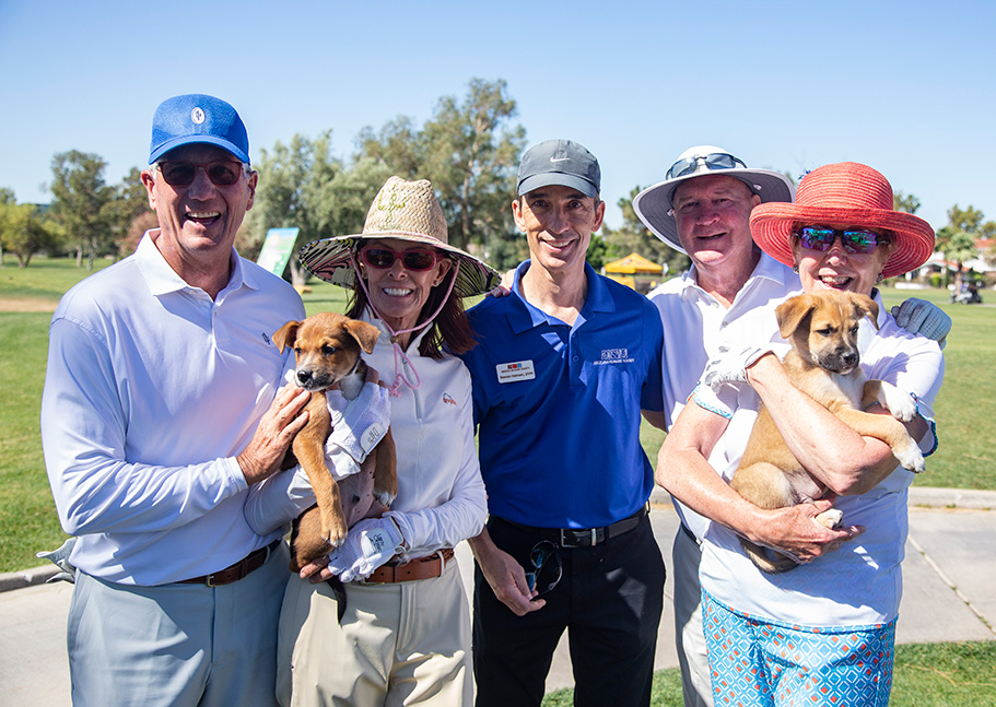 Five people hold puppies at a golf event
