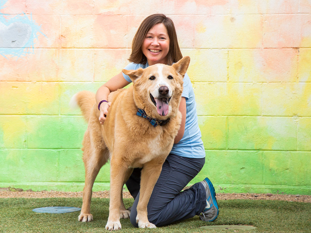 A woman poses with a dog in front of a painted wall