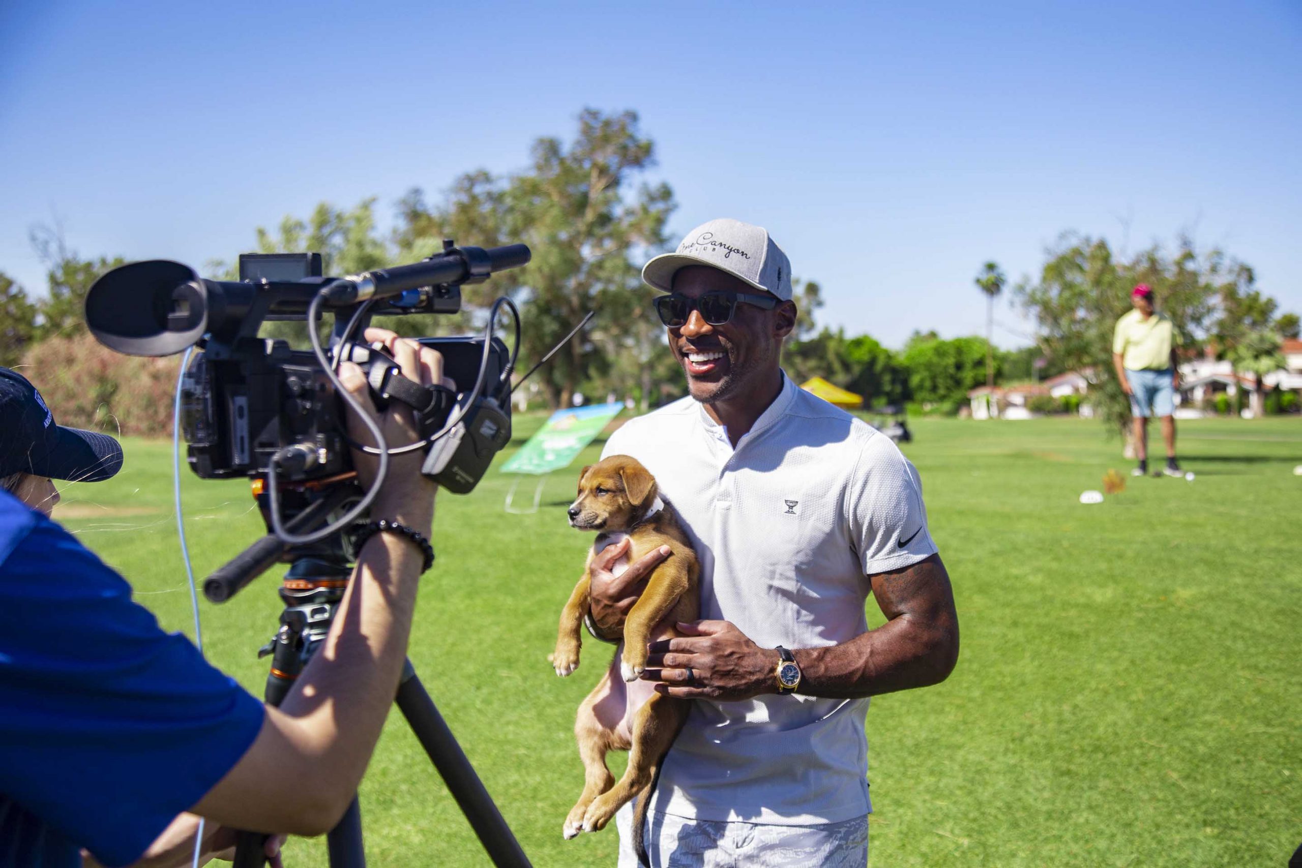 man holding puppy in front of a camera at a golf course